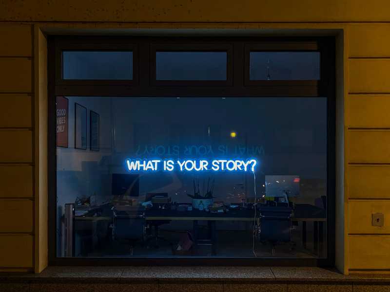 A store with a neon sign that says, "What is your story?"